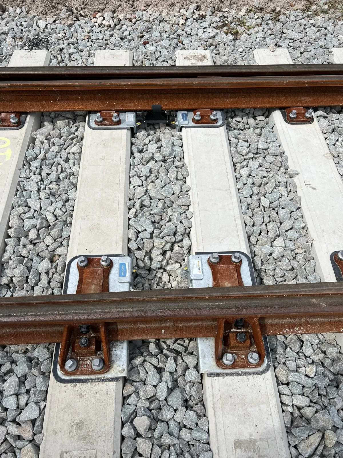 DeltaSwitch devices installed in ballasted track, one on each switch rail between the concrete bearers